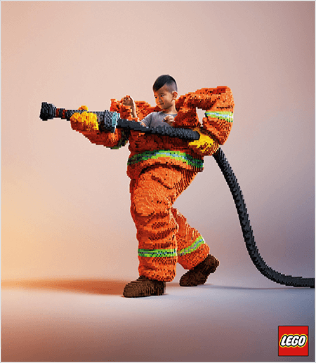 Detta är ett foto från en LEGO-annons som visar en ung asiatisk pojke inuti en brandmanuniform gjord av LEGO. Uniformen är orange med en neongrön rand runt manschetten på kappan och byxorna. Brandmannen står med en fot bak och håller en eldslang, även gjord av legos. Pojkens huvud dyker upp ur uniformens överdel, som är mycket större än han och stannar runt axlarna. Fotoet togs mot en vanlig neutral bakgrund. LEGO-logotypen visas i en röd ruta längst ned till höger. Talia Wolf säger att LEGO är ett bra exempel på ett varumärke som använder känslor i reklam.